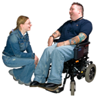 Two young people chatting. One person is sitting in a wheelchair and the other person is crouching down next to him.