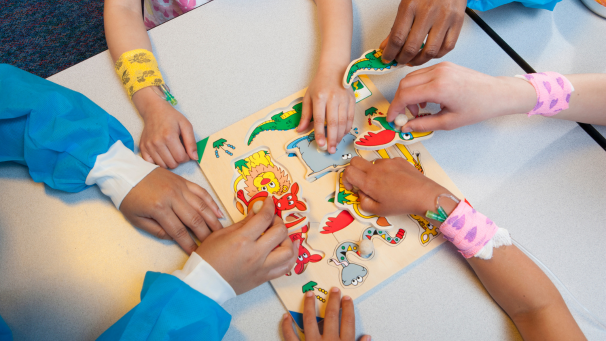 Image showing children's hands doing a wooden puzzle together in a healthcare setting